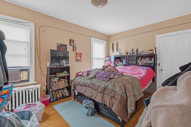 bedroom featuring radiator heating unit, wood finished floors, and cooling unit
