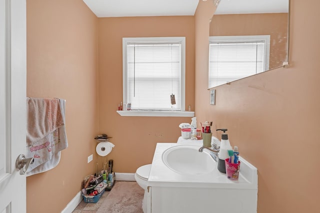 half bathroom with baseboards, toilet, and vanity