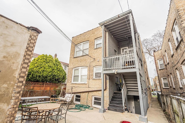 rear view of house featuring fence, stairs, brick siding, a patio, and a balcony