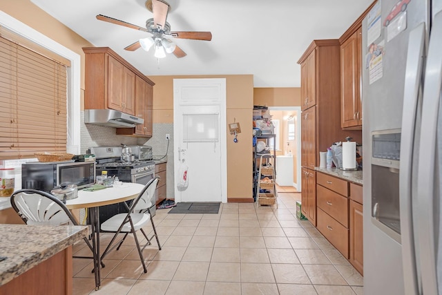 kitchen with appliances with stainless steel finishes, under cabinet range hood, a ceiling fan, light tile patterned floors, and decorative backsplash