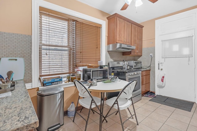 kitchen featuring appliances with stainless steel finishes, under cabinet range hood, a ceiling fan, light tile patterned floors, and tasteful backsplash