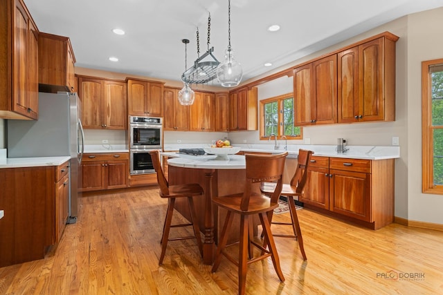 kitchen featuring appliances with stainless steel finishes, brown cabinets, a kitchen island, light countertops, and recessed lighting