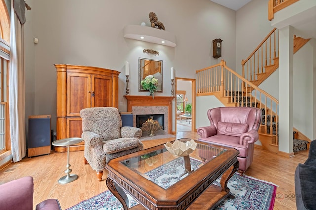 living room with a towering ceiling, stairs, light wood finished floors, a high end fireplace, and baseboards