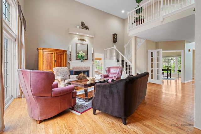 living area with a towering ceiling, a high end fireplace, light wood finished floors, stairs, and baseboards