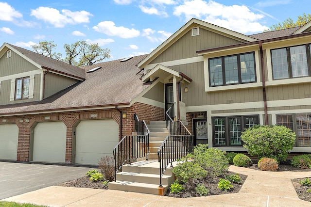 townhome / multi-family property with a shingled roof, brick siding, driveway, and an attached garage