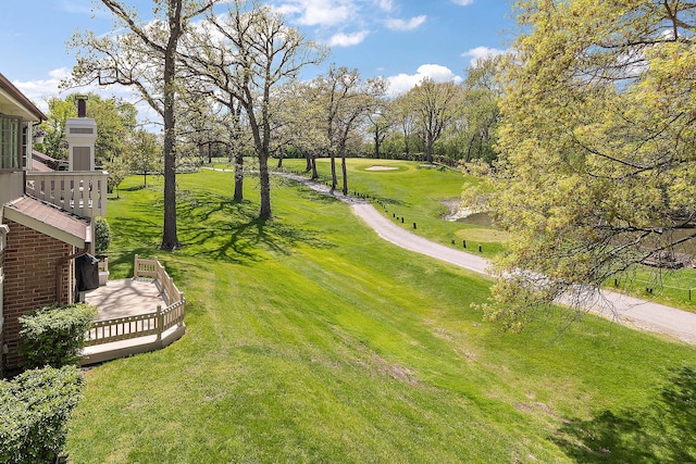 view of green lawn featuring view of golf course and view of wooded area