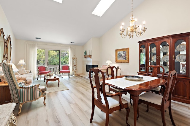 dining space with light wood-style floors, a fireplace, a skylight, a chandelier, and high vaulted ceiling