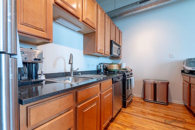 kitchen with stainless steel appliances, a sink, light wood-style floors, brown cabinets, and dark stone countertops