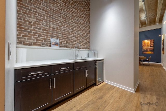 bar with a sink, brick wall, light wood-style flooring, and baseboards