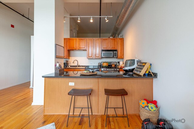 kitchen with stainless steel microwave, stove, a kitchen bar, light wood-type flooring, and a towering ceiling