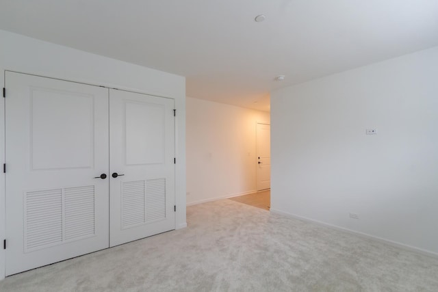 unfurnished bedroom with light carpet, a closet, and baseboards