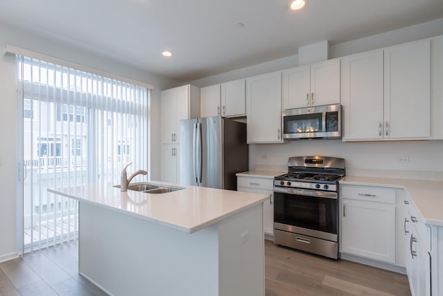 kitchen with stainless steel appliances, a sink, light wood-type flooring, a center island with sink, and light countertops