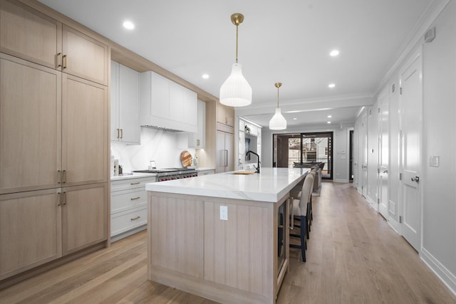 kitchen with a sink, a kitchen island with sink, ornamental molding, light wood finished floors, and paneled built in refrigerator