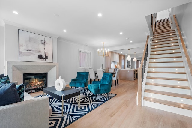living area featuring stairs, crown molding, light wood-style flooring, a high end fireplace, and a chandelier