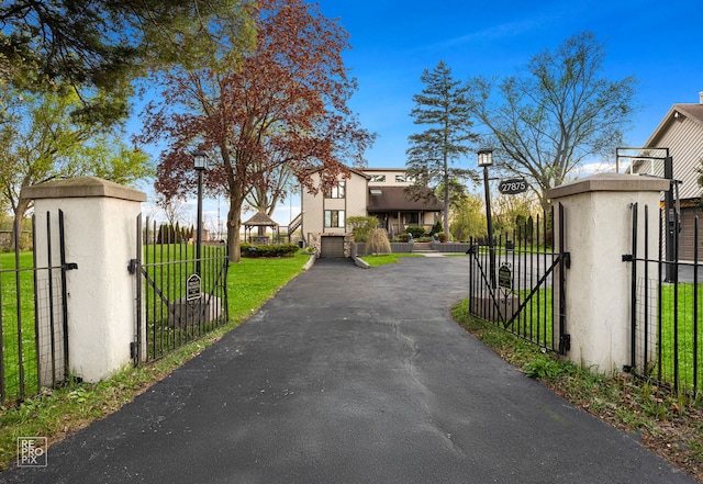 view of asphalt driveway featuring street lights, a gated entry, and a gate