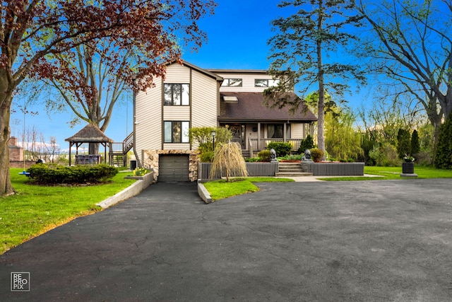 view of front of property with stone siding, an attached garage, asphalt driveway, a gazebo, and stairway