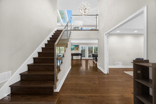 foyer entrance featuring stairway, a chandelier, a towering ceiling, wood finished floors, and baseboards