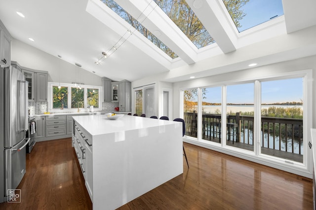 kitchen featuring gray cabinets, a skylight, freestanding refrigerator, a water view, and tasteful backsplash