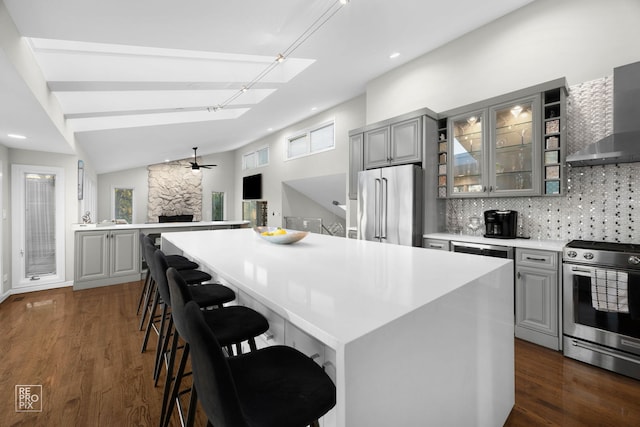 kitchen featuring gray cabinetry, appliances with stainless steel finishes, wall chimney range hood, ceiling fan, and recessed lighting