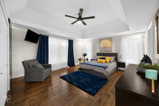 bedroom with a raised ceiling, hardwood / wood-style flooring, a ceiling fan, and baseboards