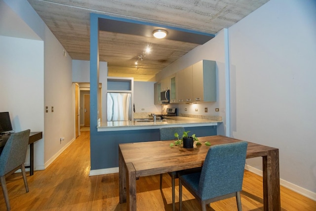 kitchen with appliances with stainless steel finishes, a peninsula, light wood-type flooring, and baseboards