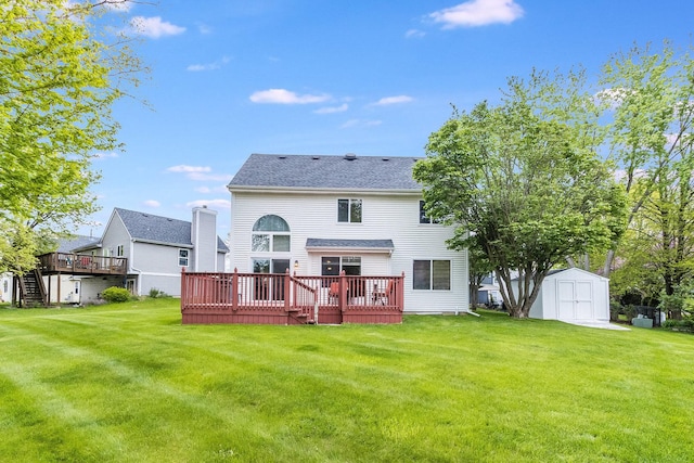 rear view of property featuring a storage shed, a wooden deck, an outdoor structure, a lawn, and a shingled roof