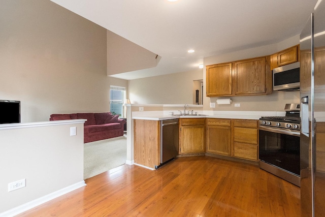 kitchen featuring appliances with stainless steel finishes, a peninsula, open floor plan, light wood-type flooring, and brown cabinets