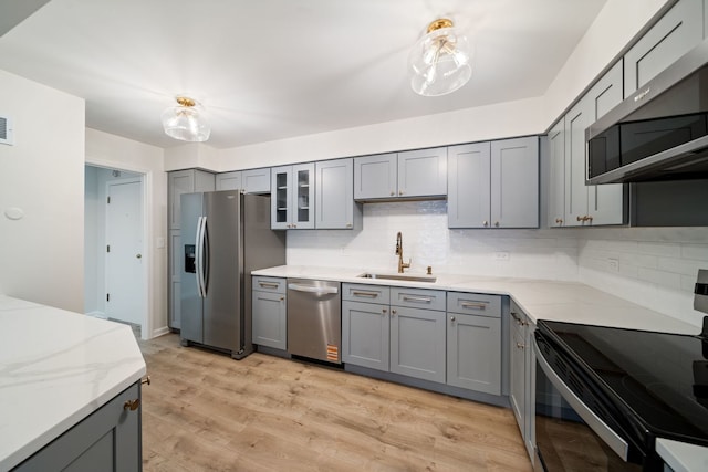 kitchen featuring stainless steel appliances, a sink, gray cabinetry, and tasteful backsplash
