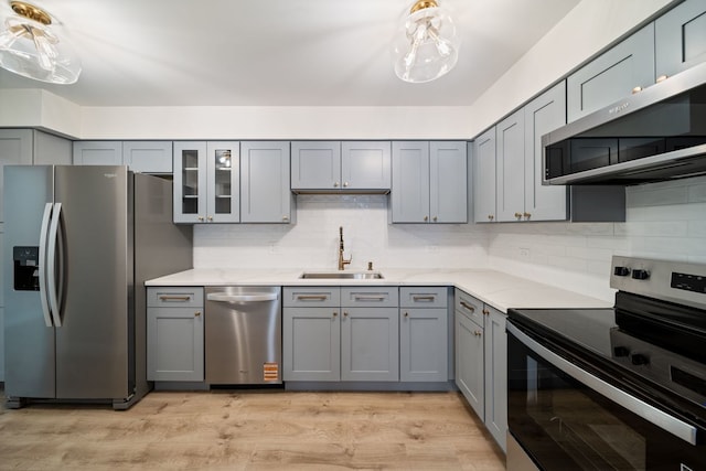 kitchen featuring stainless steel appliances, a sink, gray cabinetry, and backsplash