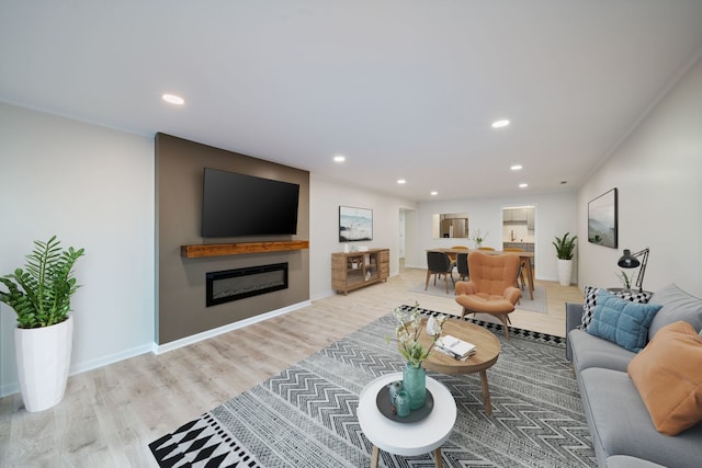 living room featuring a glass covered fireplace, recessed lighting, wood finished floors, and baseboards