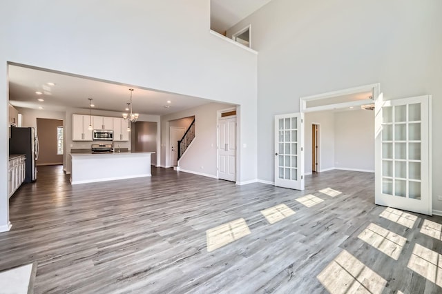 unfurnished living room with french doors, a chandelier, stairs, wood finished floors, and a towering ceiling