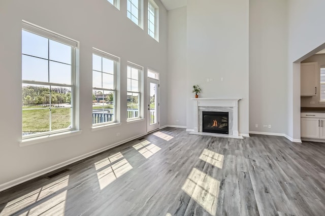 unfurnished living room with a high ceiling, baseboards, wood finished floors, and a fireplace