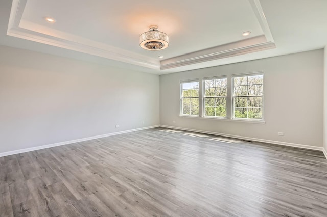 unfurnished room featuring a raised ceiling, recessed lighting, baseboards, and wood finished floors