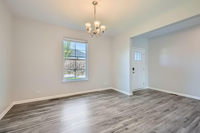 unfurnished room with a chandelier, wood finished floors, and baseboards