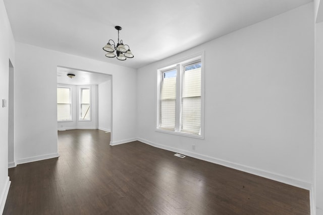unfurnished dining area with a chandelier, healthy amount of natural light, dark wood-style flooring, and baseboards