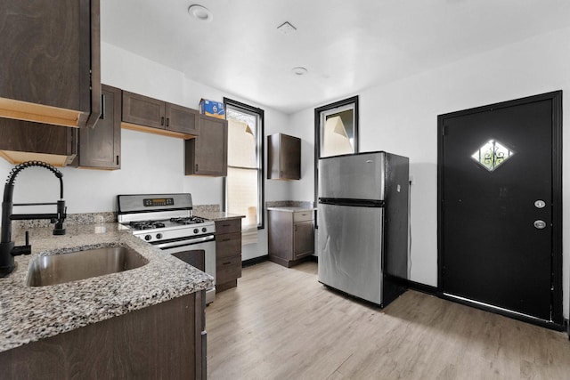kitchen with stainless steel appliances, a sink, light wood-style floors, dark brown cabinets, and light stone counters
