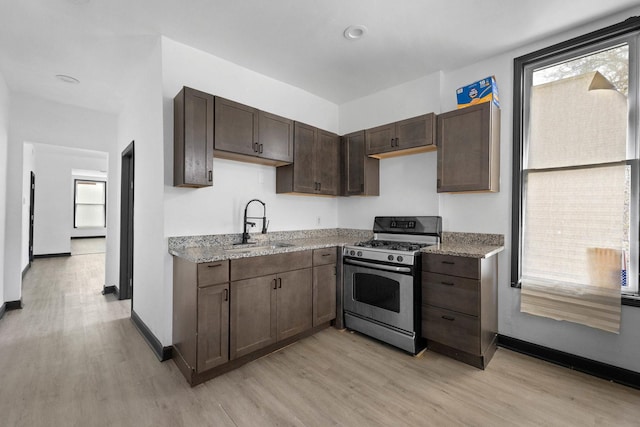 kitchen with stainless steel gas range oven, a sink, light wood-type flooring, and dark brown cabinets