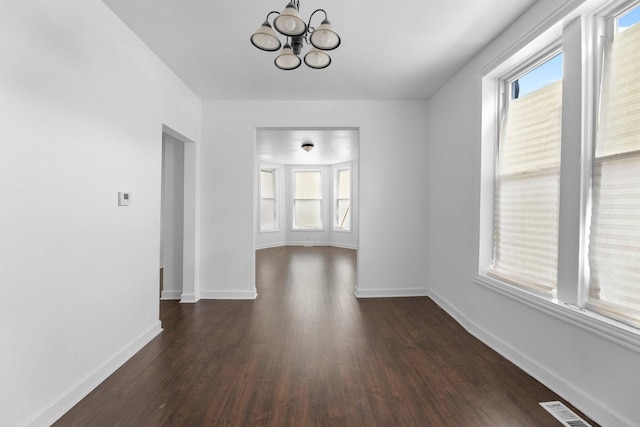 unfurnished dining area with dark wood-type flooring, a chandelier, and baseboards