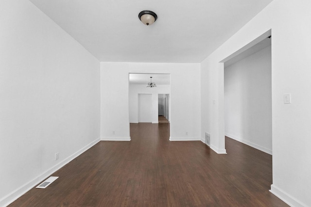 spare room featuring dark wood-style flooring, baseboards, and a chandelier