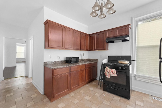 kitchen featuring black appliances, under cabinet range hood, light stone finish flooring, a chandelier, and baseboards