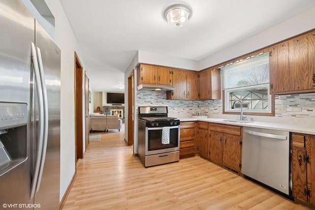 86 Brookside Dr, Elgin, IL 60123 - kitchen featuring appliances with stainless steel finishes, a sink, under cabinet range hood, brown cabinets, and tasteful backsplash