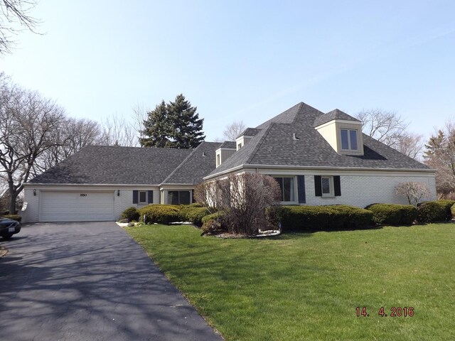 view of front of property featuring asphalt driveway, brick siding, an attached garage, and a front lawn