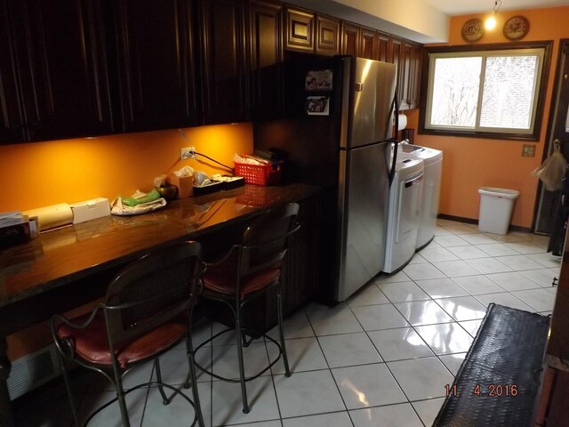 kitchen with light tile patterned floors, washer and clothes dryer, dark countertops, a kitchen breakfast bar, and freestanding refrigerator