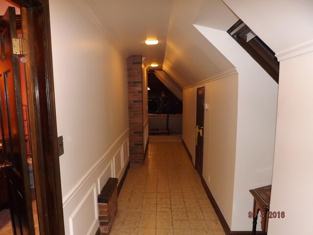 corridor with crown molding, vaulted ceiling, and a decorative wall
