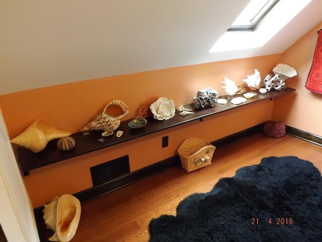 playroom with wood finished floors, a skylight, vaulted ceiling, and baseboards