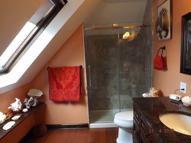 full bathroom with a skylight, a stall shower, toilet, vanity, and wood finished floors