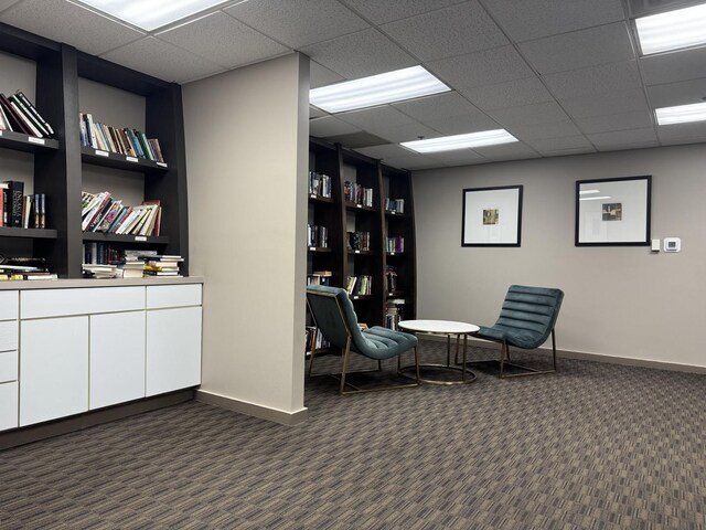 living area with dark carpet, a drop ceiling, and baseboards