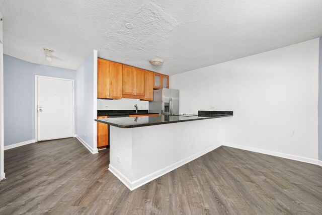 kitchen with stainless steel refrigerator with ice dispenser, dark wood-style flooring, baseboards, a peninsula, and a textured ceiling
