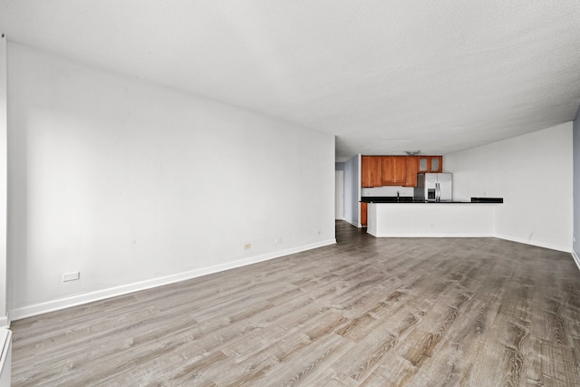 unfurnished living room featuring wood finished floors, baseboards, and a baseboard heating unit