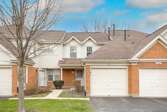 townhome / multi-family property featuring driveway, a shingled roof, brick siding, and an attached garage